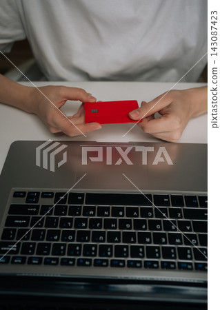 Vertical cropped shot of person holding red credit card while using laptop computer, representing online shopping, financial transactions, secure electronic payment through e-commerce platforms. Vertical cropped shot of person holding red credit card while using laptop computer, representing online shopping, financial transactions, secure electronic payment through e-commerce platforms. 143087423