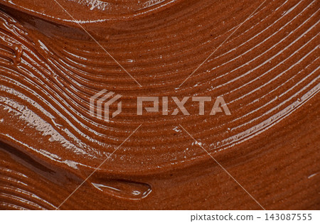 Smooth, rich chocolate spread with glossy texture and swirling patterns on a flat surface, showcasing its creamy consistency and appetizing appearance 143087555
