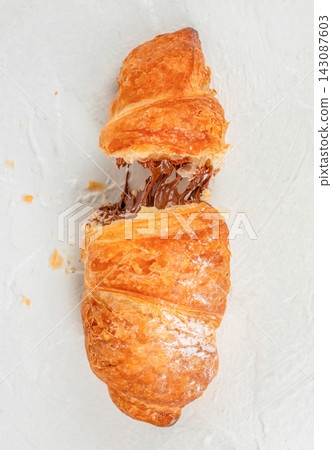 Freshly baked croissant with melted chocolate filling, partially broken to reveal rich, gooey chocolate inside on a light textured background Freshly baked croissant with melted chocolate filling, partially broken to reveal rich, gooey chocolate inside on a light textured background 143087603