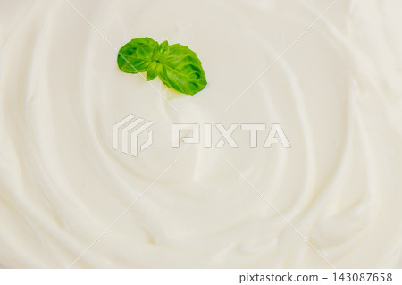 Creamy white sauce with a fresh green basil leaf placed in the center, showcasing a smooth texture and swirls on a white background Creamy white sauce with a fresh green basil leaf placed in the center, showcasing a smooth texture and swirls on a white background 143087658