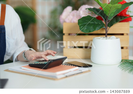 Cropped hand using calculator at desk for small business accounting and finance Cropped hand using calculator at desk for small business accounting and finance 143087889