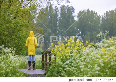 Young woman with yellow raincoat and rubber boots in spring nature Young woman with yellow raincoat and rubber boots in spring nature 143088767