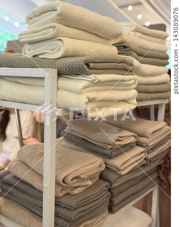 Stacked beige towels and knitted blankets displayed on retail shelving in a cozy home goods store 143089076
