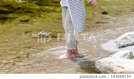 Splashes of water fly around the feet of a woman walking in the shallow part of the river. Splashes of water fly around the feet of a woman walking in the shallow part of the river. 143089134
