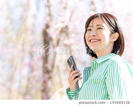 A woman holding a smartphone in the dappled sunlight of spring. A woman holding a smartphone in the dappled sunlight of spring. 143089136