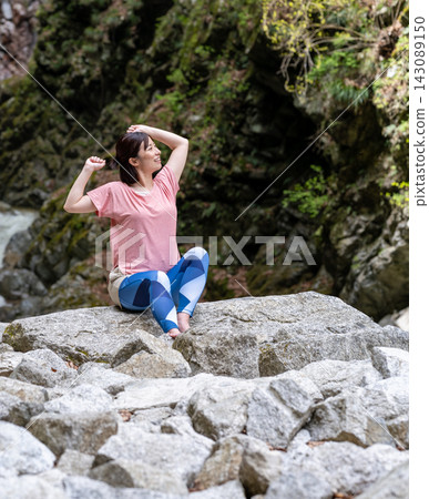 一位女子坐在岩石上整理頭髮。 143089150