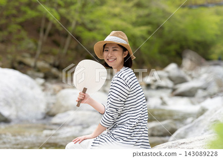 A woman holding a fan by the river. A woman holding a fan by the river. 143089228