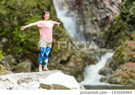 A woman with her arms outstretched in front of a waterfall A woman with her arms outstretched in front of a waterfall 143089464