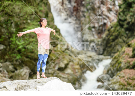 A woman with her arms outstretched in front of a waterfall A woman with her arms outstretched in front of a waterfall 143089477
