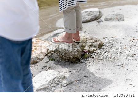 A woman's feet wearing sandals on a rock by the river. A woman's feet wearing sandals on a rock by the river. 143089481