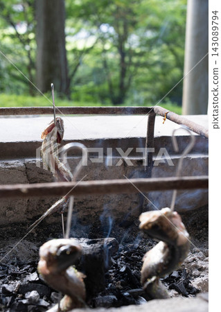 以森林為背景的烤魚串在炭火上烤製。 以森林為背景的烤魚串在炭火上烤製。 143089794
