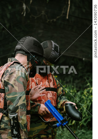 Paintball Players Strategizing Outdoors in Camouflage Gear Paintball Players Strategizing Outdoors in Camouflage Gear 143090736