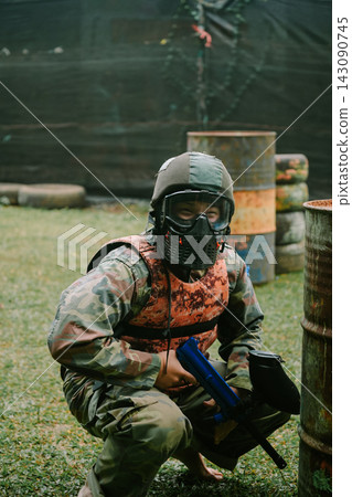 Paintball player crouching behind a metal barrel during tactical game Paintball player crouching behind a metal barrel during tactical game 143090745