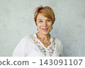 Joyful elegant senior woman wearing casual white shirt standing over grey background 143091107