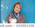 Portrait of mature woman with short hair standing outdoors against blue wall background 143091108