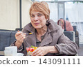 Cute senior woman eating dessert while sitting in city street cafe 143091111