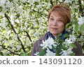 Beautiful senior woman with short hair smiling and enjoying spring apple flowers  143091120