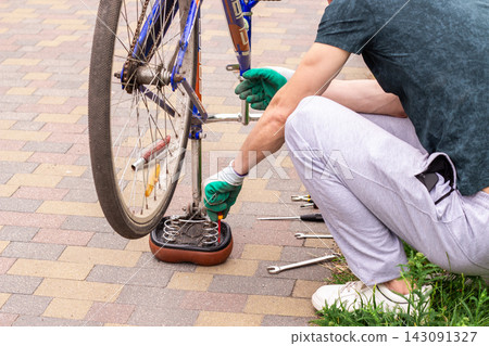 Man examining bike chain and gears for wear. Upside down position reveals issues. Practical competence outside house Man examining bike chain and gears for wear. Upside down position reveals issues. Practical competence outside house 143091327