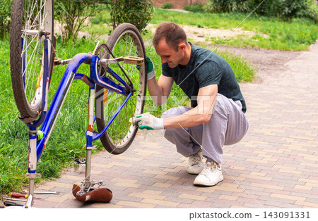 Man washing bike after keeping it in basement during cold days. Keeping transport clean and functional. Hands on approach to property care. Seasonal bicycle preparation for summer Man washing bike after keeping it in basement during cold days. Keeping transport clean and functional. Hands on approach to property care. Seasonal bicycle preparation for summer 143091331