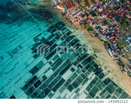 Drone view of turquoise coastal aquaculture farms beside a tropical seaside village Drone view of turquoise coastal aquaculture farms beside a tropical seaside village 143091522
