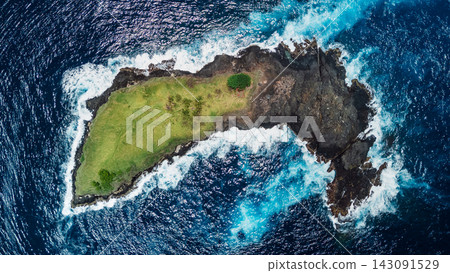 Above view of a small green rocky island surrounded by deep blue ocean Above view of a small green rocky island surrounded by deep blue ocean 143091529