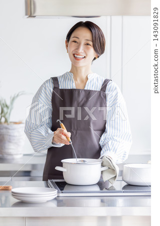 一位日本女教師在烹飪課上一邊攪拌鍋裡的食材一邊微笑。 一位日本女教師在烹飪課上一邊攪拌鍋裡的食材一邊微笑。 143091829