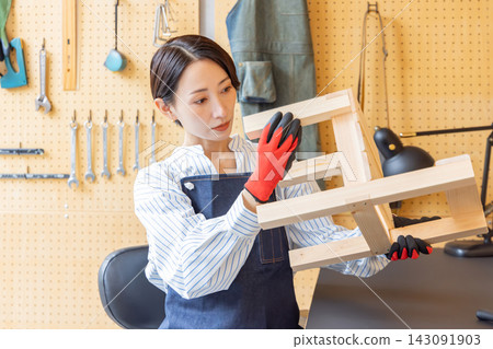 一位日本女性正在檢查她在DIY工作室裡製作的木椅。 一位日本女性正在檢查她在DIY工作室裡製作的木椅。 143091903