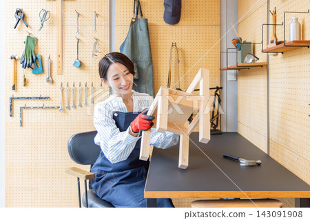 一位日本女性正在檢查她在DIY工作室裡製作的木椅。 一位日本女性正在檢查她在DIY工作室裡製作的木椅。 143091908