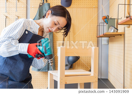 一位日本女子在DIY工作室用電鑽組裝一張木椅。 一位日本女子在DIY工作室用電鑽組裝一張木椅。 143091909