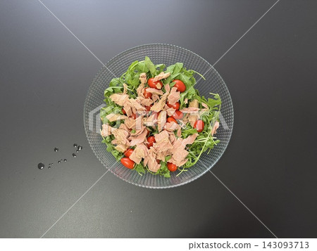 Top view of arugula salad with cherry tomatoes and canned tuna in glass bowl on dark table. Healthy protein meal and Mediterranean dietary concept. Top view of arugula salad with cherry tomatoes and canned tuna in glass bowl on dark table. Healthy protein meal and Mediterranean dietary concept. 143093713