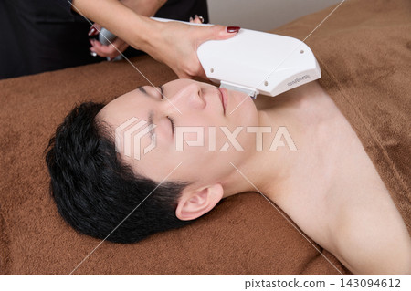 A man receiving facial hair removal treatment from a beauty staff member. A man receiving facial hair removal treatment from a beauty staff member. 143094612