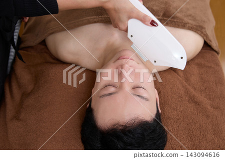 A man receiving facial hair removal treatment from a beauty staff member. A man receiving facial hair removal treatment from a beauty staff member. 143094616