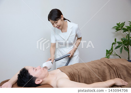 A beauty staff member applies a hair removal device to a man's underarms during the procedure. A beauty staff member applies a hair removal device to a man's underarms during the procedure. 143094706