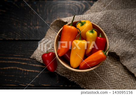 Colorful mini sweet peppers in a wooden bowl on rustic burlap and dark timber background. Colorful mini sweet peppers in a wooden bowl on rustic burlap and dark timber background. 143095156