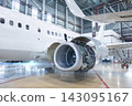 White passenger aircraft with open high bypass turbofan airplane engine in aviation hangar. Plane under maintenance. Checking mechanical systems for flight operations 143095167
