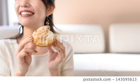 一位女士面帶微笑,手裡拿著一個奶油泡芙。 一位女士面帶微笑,手裡拿著一個奶油泡芙。 143095613