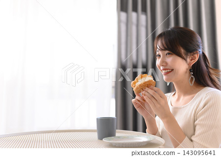 A woman smiles and eats a cream puff in her hand. A woman smiles and eats a cream puff in her hand. 143095641