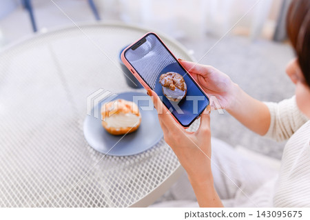 A woman's hands as she takes a picture of a cream puff with her smartphone. 143095675