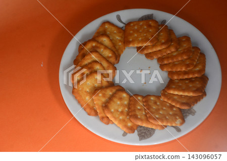 Crispy golden square crackers arranged neatly in a circle on a white patterned Crispy golden square crackers arranged neatly in a circle on a white patterned 143096057