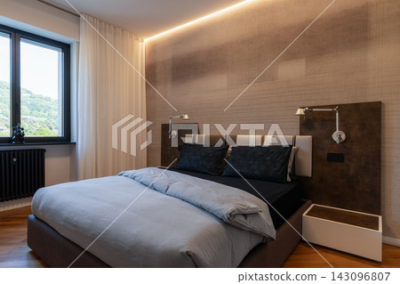 Contemporary primary bedroom with upholstered bed and warm indirect lighting 143096807
