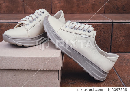 Minimalist eco-friendly white sneakers placed on recycled cardboard box, clean design for sustainable fashion concepts. New unbranded beige sneakers footwear mockups and modern product displays. For Minimalist eco-friendly white sneakers placed on recycled cardboard box, clean design for sustainable fashion concepts. New unbranded beige sneakers footwear mockups and modern product displays. For 143097238