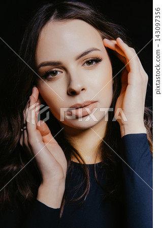 Fashion model posing touching her face with hands on black background Fashion model posing touching her face with hands on black background 143097356
