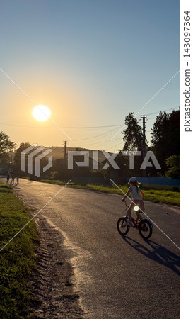 Young girl cycling on rural road at sunset Young girl cycling on rural road at sunset 143097364