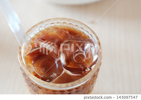 Cold iced coffee served in a glass with cubes and a straw Cold iced coffee served in a glass with cubes and a straw 143097547
