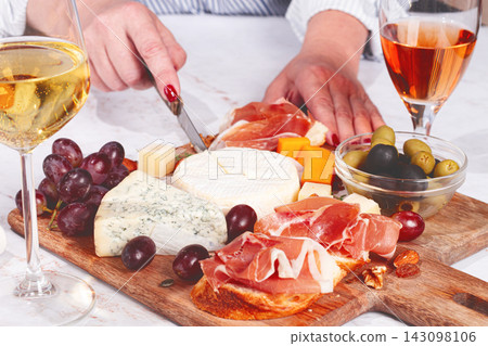 Sharing a cheese board with grapes, meats, and drinks during a gathering at home Sharing a cheese board with grapes, meats, and drinks during a gathering at home 143098106