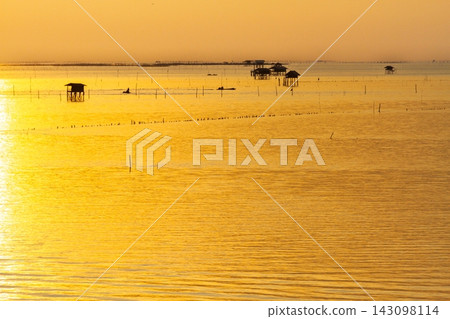 Golden sunset over the calm sea with traditional stilt houses and small fishing boats at dusk Golden sunset over the calm sea with traditional stilt houses and small fishing boats at dusk 143098114