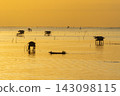 Golden sunset over calm water with fishing huts and traditional boat 143098115