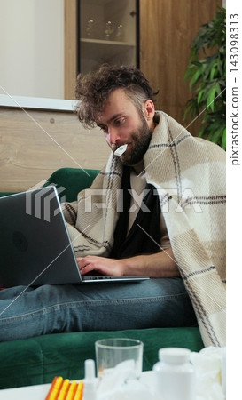 Vertical video. Sick male freelancer sitting on sofa at home office under plaid, working remotely, using paper tissue with thermometer in mouth. Man feeling unwell, sick with running nose, need a rest Vertical video. Sick male freelancer sitting on sofa at home office under plaid, working remotely, using paper tissue with thermometer in mouth. Man feeling unwell, sick with running nose, need a rest 143098313