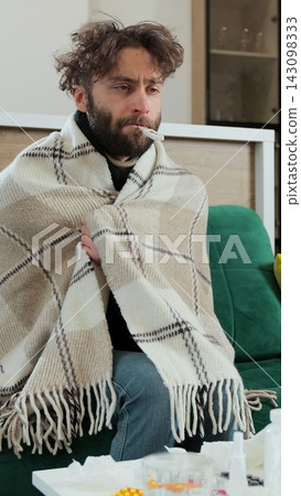 Vertical video. Man covered with a warm plaid measuring a temperature and having a thermometer in his mouth. Guy catch a cold, influenza virus symptoms, grippe and flue, need care and treatment Vertical video. Man covered with a warm plaid measuring a temperature and having a thermometer in his mouth. Guy catch a cold, influenza virus symptoms, grippe and flue, need care and treatment 143098333
