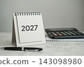 2027 desk calendar with pen, calculator and notepad on desktop. Financial planning, budgeting, corporate goals, tax planning concept 143098980